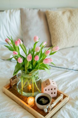 Bahar dekoru, vazoda bir buket lale, tahta tepside sıcak kahve. Yatakta kahvaltı. Yatak odasının içi..