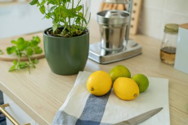 Bej ışıklı mutfakta ev yapımı limonata yapıyorum. Tahtada limon ve limon, kavanozda nane şekeri. Meyve sıkacağı.