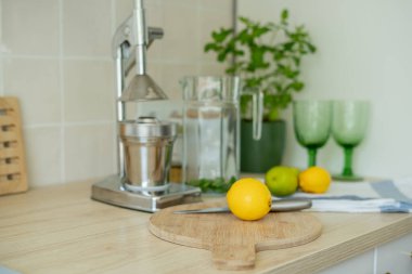 Bej ışıklı mutfakta ev yapımı limonata yapıyorum. Tahtada limon ve limon, kavanozda nane şekeri. Meyve sıkacağı.