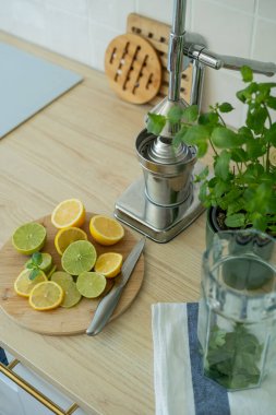 Bej ışıklı mutfakta ev yapımı limonata yapıyorum. Tahtada limon ve limon, kavanozda nane şekeri. Meyve sıkacağı.