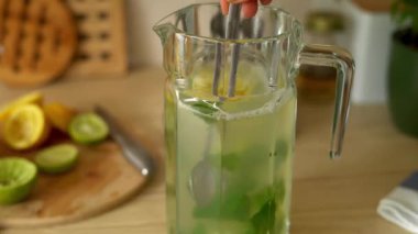 Ev yapımı limonata için limon, nane ve böğürtlen hazırlayan kadın ellerine yakın çekim. Parlak mutfakta soğuk yaz içkisi hazırlayan genç bir kadın..
