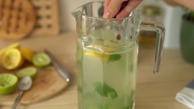 Ev yapımı limonata için limon, nane ve böğürtlen hazırlayan kadın ellerine yakın çekim. Parlak mutfakta soğuk yaz içkisi hazırlayan genç bir kadın..