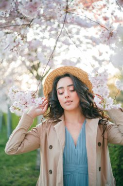 36 yaşında, kıvırcık, uzun siyah saçlı güzel bir kadın gün batımında çiçek açan sakura 'nın yanında. Baharda çiçek açan parkta mavi elbiseli bir model..