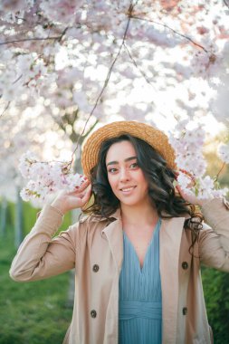36 yaşında, kıvırcık, uzun siyah saçlı güzel bir kadın gün batımında çiçek açan sakura 'nın yanında. Baharda çiçek açan parkta mavi elbiseli bir model..