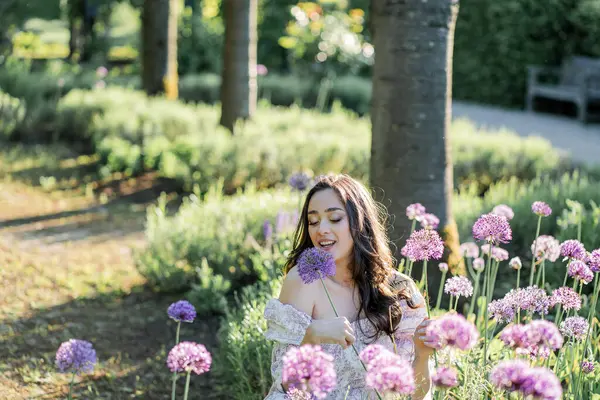 Parktaki çiçeklerin yanında siyah saçlı genç bir kadının portresi. Romantik bir elbisenin içinde baharda sevinen mutlu bir manken..