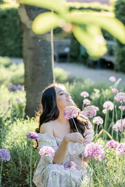 Parktaki çiçeklerin yanında siyah saçlı genç bir kadının portresi. Romantik bir elbisenin içinde baharda sevinen mutlu bir manken..