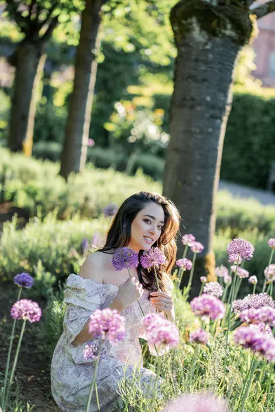 Parktaki çiçeklerin yanında siyah saçlı genç bir kadının portresi. Romantik bir elbisenin içinde baharda sevinen mutlu bir manken..