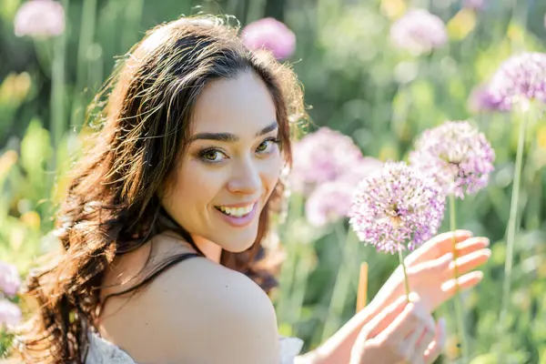 Parktaki çiçeklerin yanında siyah saçlı genç bir kadının portresi. Romantik bir elbisenin içinde baharda sevinen mutlu bir manken..