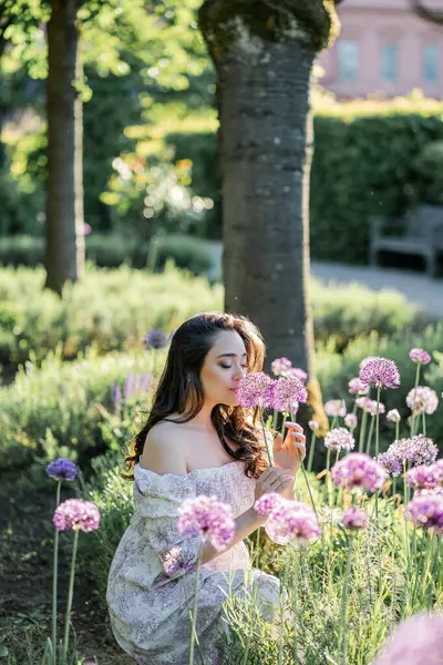 Parktaki çiçeklerin yanında siyah saçlı genç bir kadının portresi. Romantik bir elbisenin içinde baharda sevinen mutlu bir manken..