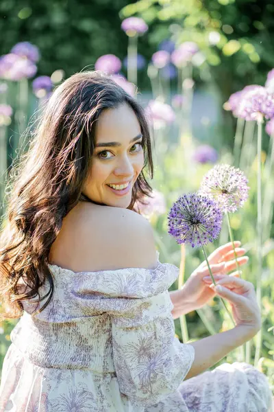 Parktaki çiçeklerin yanında siyah saçlı genç bir kadının portresi. Romantik bir elbisenin içinde baharda sevinen mutlu bir manken..