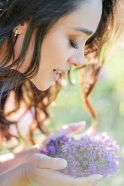 Parktaki çiçeklerin yanında siyah saçlı genç bir kadının portresi. Romantik bir elbisenin içinde baharda sevinen mutlu bir manken..