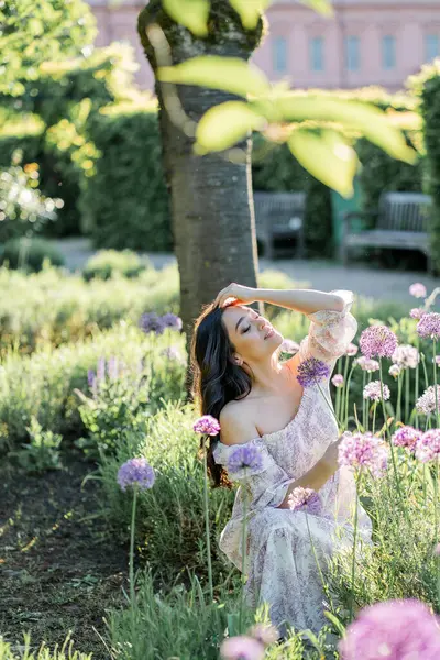 Parktaki çiçeklerin yanında siyah saçlı genç bir kadının portresi. Romantik bir elbisenin içinde baharda sevinen mutlu bir manken..