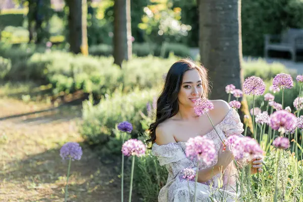 Parktaki çiçeklerin yanında siyah saçlı genç bir kadının portresi. Romantik bir elbisenin içinde baharda sevinen mutlu bir manken..