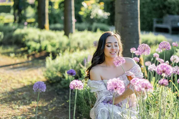 Parktaki çiçeklerin yanında siyah saçlı genç bir kadının portresi. Romantik bir elbisenin içinde baharda sevinen mutlu bir manken..