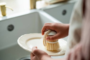 Mutfaktaki lavabonun yanında bir tabak yıkayan çocukların elleri. Küçük kız elinde bir bulaşık fırçası tutuyor..