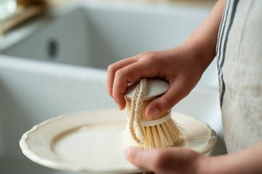Mutfaktaki lavabonun yanında bir tabak yıkayan çocukların elleri. Küçük kız elinde bir bulaşık fırçası tutuyor..