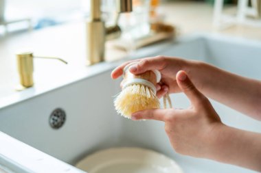 Mutfaktaki lavabonun yanında bir tabak yıkayan çocukların elleri. Küçük kız elinde bir bulaşık fırçası tutuyor..