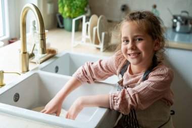 Mutfaktaki lavabonun yanında bir tabak yıkayan çocukların elleri. Küçük kız elinde bir bulaşık fırçası tutuyor..