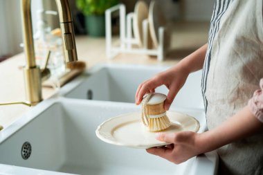 Mutfaktaki lavabonun yanında bir tabak yıkayan çocukların elleri. Küçük kız elinde bir bulaşık fırçası tutuyor..