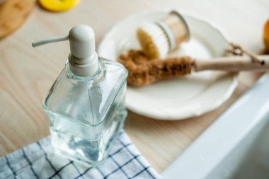 Lavabonun yanında bulaşık yıkamak için bir ekofırça, cam şişede deterjan ve havlu. Parlak mutfak iç mimarisi.