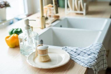 Lavabonun yanında bulaşık yıkamak için bir ekofırça, cam şişede deterjan ve havlu. Parlak mutfak iç mimarisi.