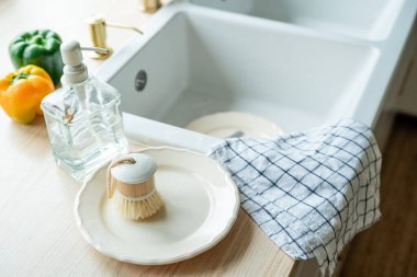 Lavabonun yanında bulaşık yıkamak için bir ekofırça, cam şişede deterjan ve havlu. Parlak mutfak iç mimarisi.