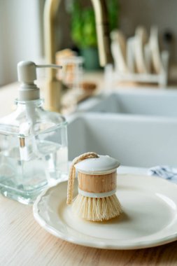 Lavabonun yanında bulaşık yıkamak için bir ekofırça, cam şişede deterjan ve havlu. Parlak mutfak iç mimarisi.