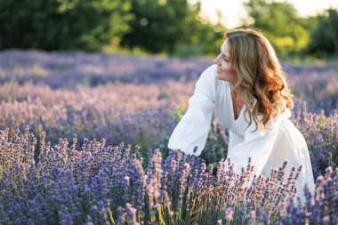 Güzel bir kadın lavanta tarlasında yaz esintisinin tadını çıkarıyor. Güneş ışığındaki sarışının portresi.