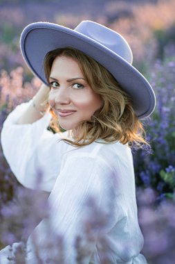 Güzel bir kadın lavanta tarlasında yaz esintisinin tadını çıkarıyor. Güneş ışığındaki sarışının portresi.