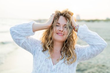 Deniz kenarındaki genç kıvırcık kadın. Kumsalda kum var. Mavi su. seyahat.