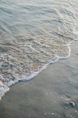 Gün batımında denize yakın. Kumsalda kum var. Mavi su.