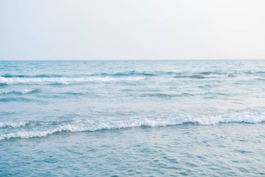 Gün batımında denize yakın. Kumsalda kum var. Mavi su.