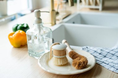 Lavabonun yanında bulaşık yıkamak için bir ekofırça, cam şişede deterjan ve havlu. Parlak mutfak iç mimarisi.