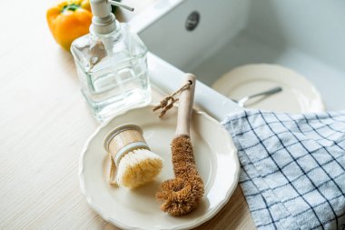 Lavabonun yanında bulaşık yıkamak için bir ekofırça, cam şişede deterjan ve havlu. Parlak mutfak iç mimarisi.