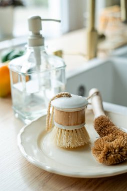 Lavabonun yanında bulaşık yıkamak için bir ekofırça, cam şişede deterjan ve havlu. Parlak mutfak iç mimarisi.