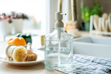 Lavabonun yanında bulaşık yıkamak için bir ekofırça, cam şişede deterjan ve havlu. Parlak mutfak iç mimarisi.