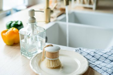 Lavabonun yanında bulaşık yıkamak için bir ekofırça, cam şişede deterjan ve havlu. Parlak mutfak iç mimarisi.