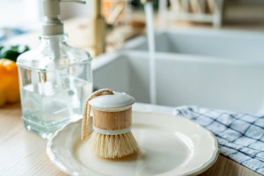 Lavabonun yanında bulaşık yıkamak için bir ekofırça, cam şişede deterjan ve havlu. Parlak mutfak iç mimarisi.