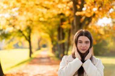Sezon. Sonbahar parkında rahat bir palto giymiş genç bir kadının portresi. Sarı yapraklar.