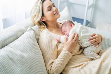 Genç anne yeni doğmuş bebeği şefkatle kucağında tutuyor. sağlıklı annelik.