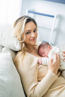 Genç anne yeni doğmuş bebeği şefkatle kucağında tutuyor. sağlıklı annelik.