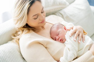 Genç anne yeni doğmuş bebeği şefkatle kucağında tutuyor. sağlıklı annelik.