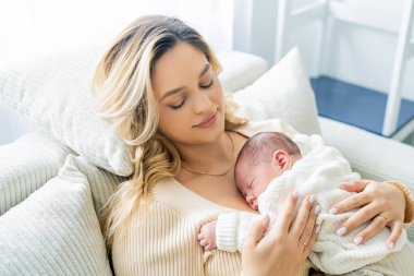 Genç anne yeni doğmuş bebeği şefkatle kucağında tutuyor. sağlıklı annelik.