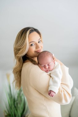 Genç anne yeni doğmuş bebeği şefkatle kucağında tutuyor. sağlıklı annelik.