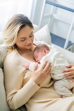 Genç anne yeni doğmuş bebeği şefkatle kucağında tutuyor. sağlıklı annelik.