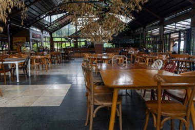 Cafe interior containing wooden tables and chairs in the middle of nature landscape