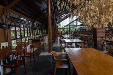 Cafe interior containing wooden tables and chairs in the middle of nature landscape
