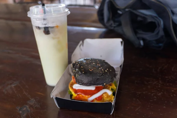 Burgers and Beverages: A Burger with Black Bun on a Wooden Table Next to a Drink