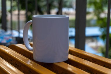 peaceful close-up of a white mug resting on a bench in a lush green park