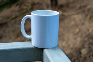 peaceful close-up of a white mug resting on a bench in a lush green park